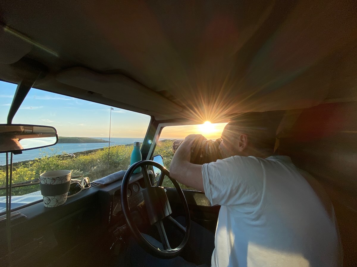 Wildlife filmmaker using a long-lens camera from a vehicle at sunset on the UK coast